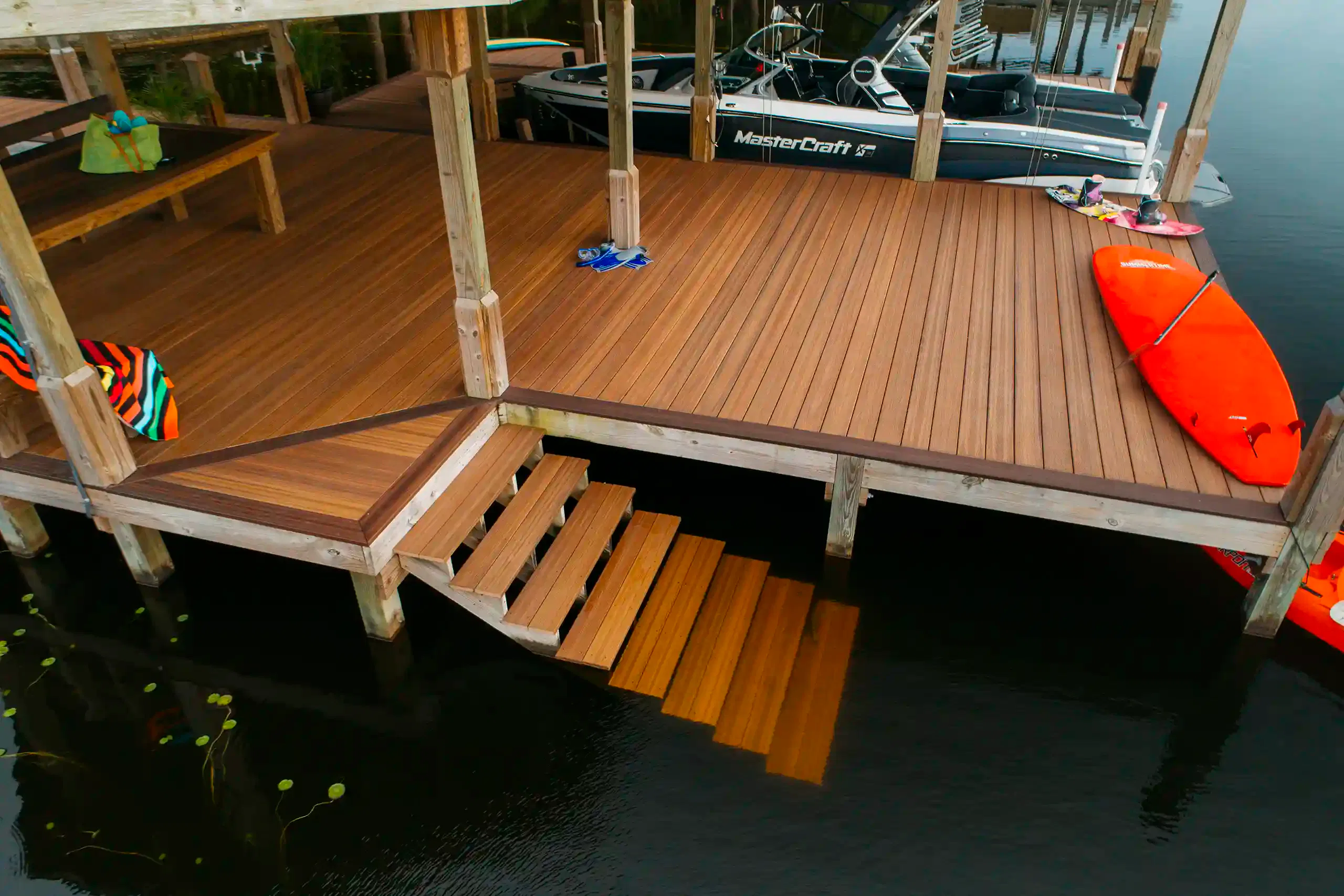 Photo of a waterfront deck with composite wood, floating stairs, and boat dock. A red kayak and MasterCraft boat are nearby.