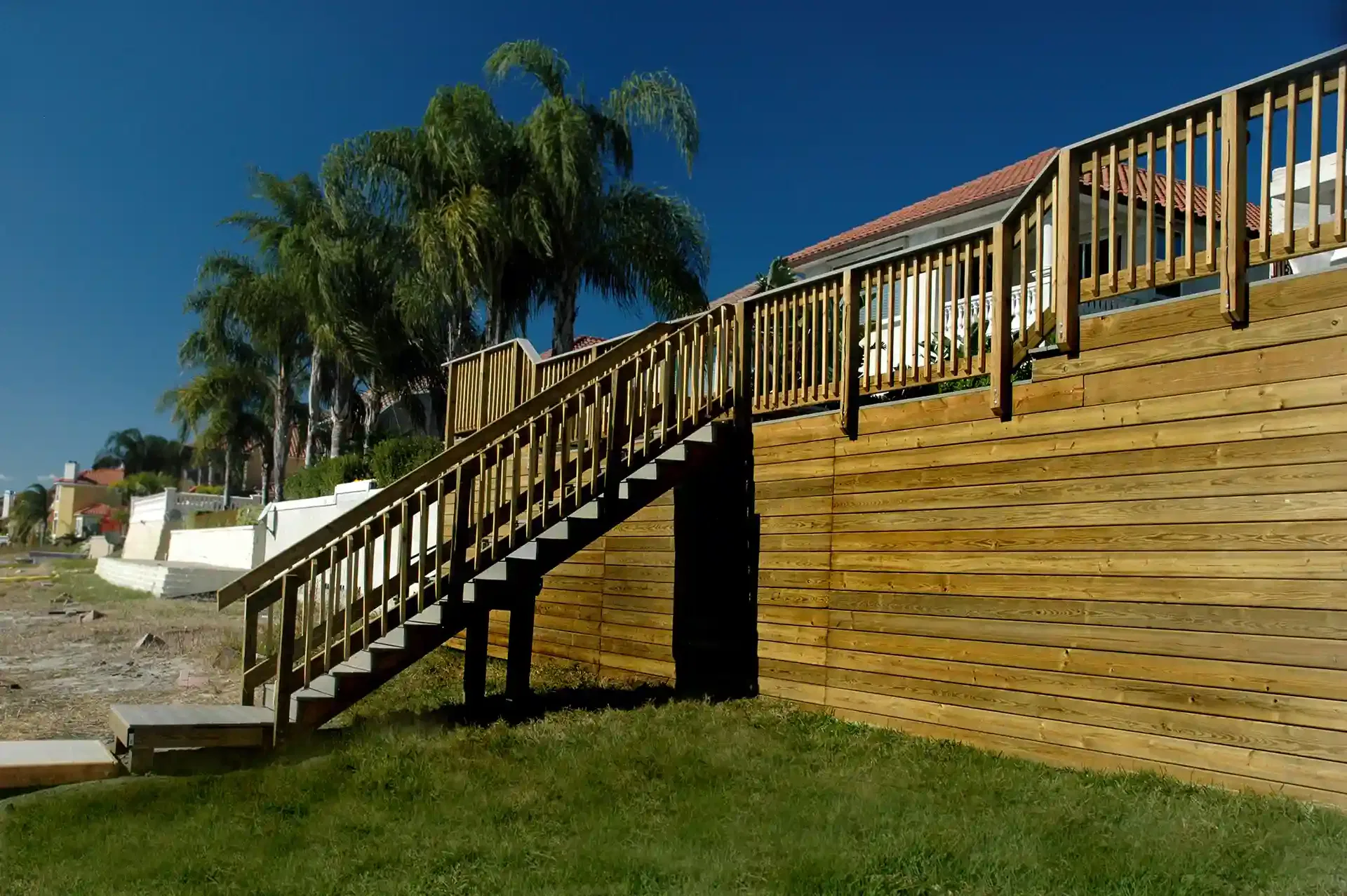 large elevated wooden deck with stairs, railing, and a retaining wall.