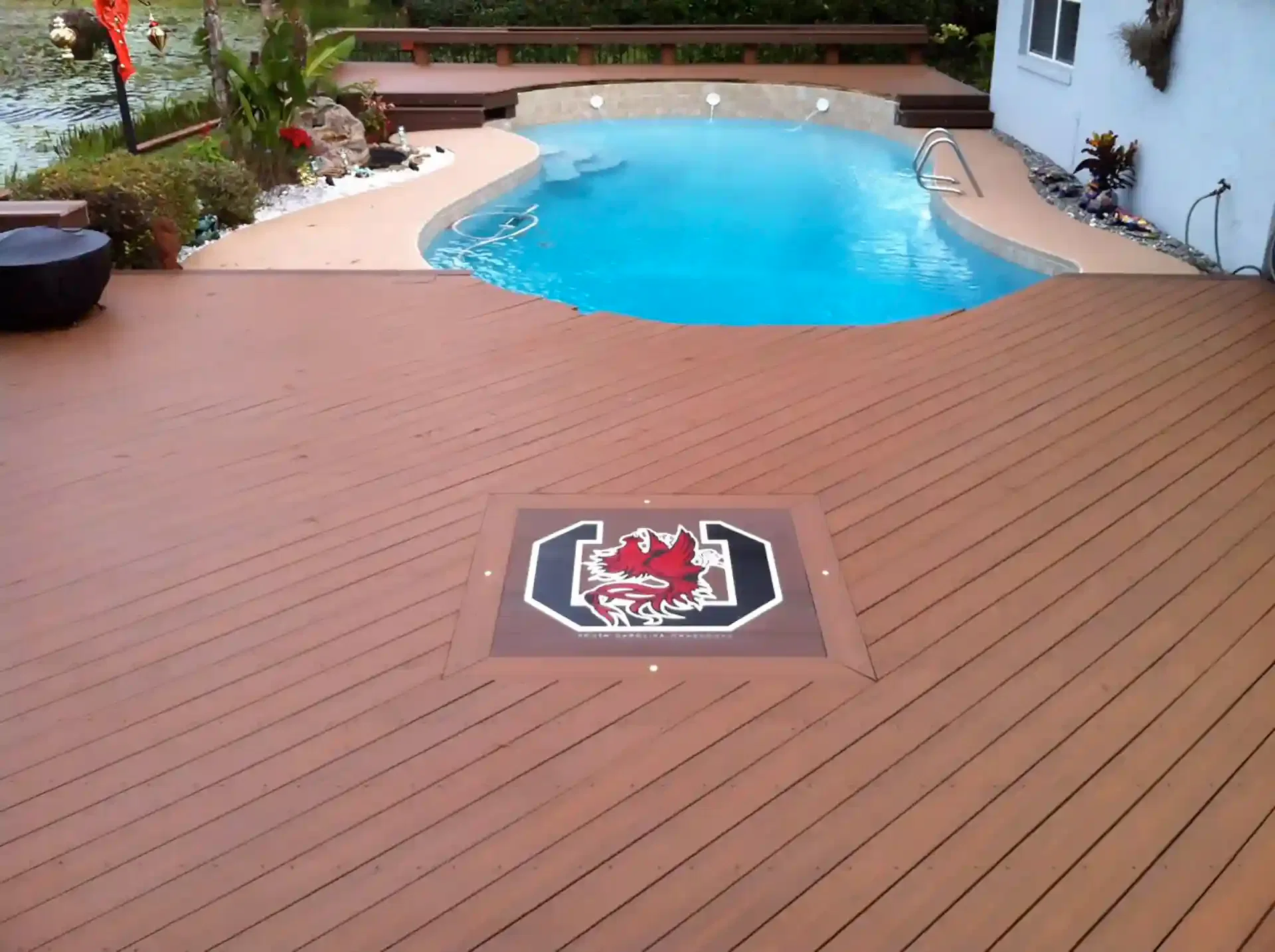 Photo of a pool deck featuring composite decking, a deck inlage, and poured concrete