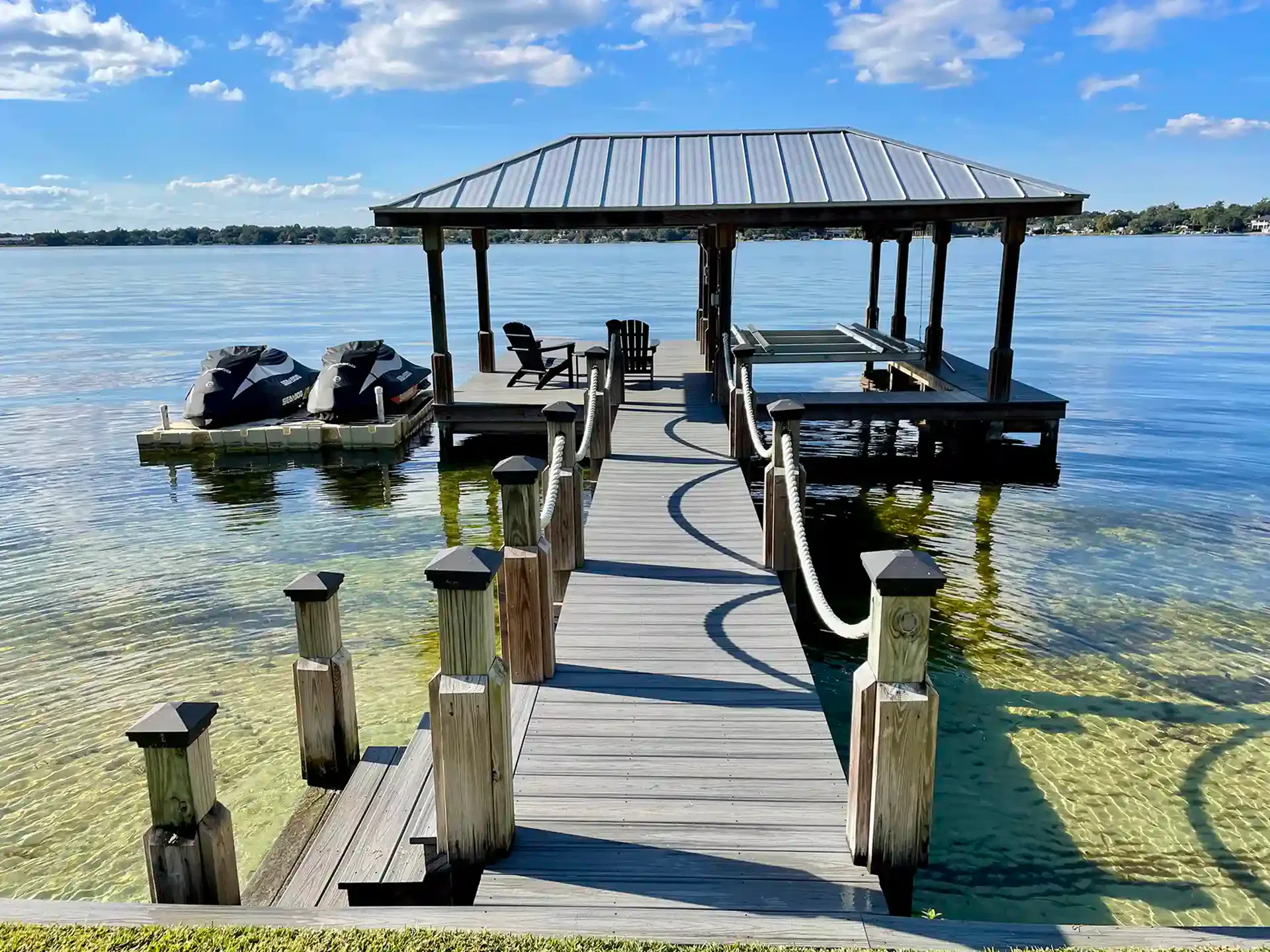 Photo of walkway leading to covered boathouse with boat lift and floating personal watercraft dock. 