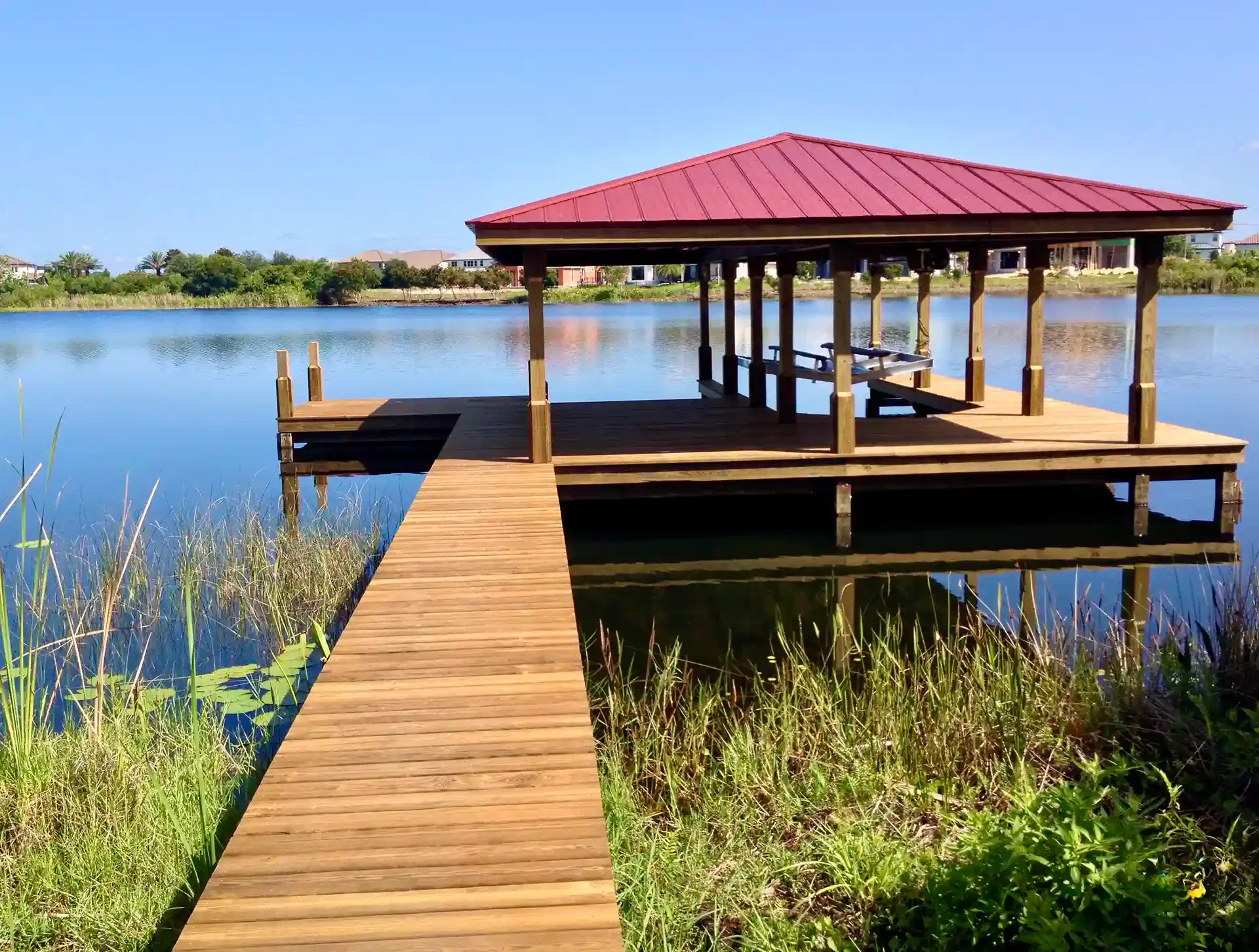 Photo of a boat house with red metal roof and walkway from land to dock.